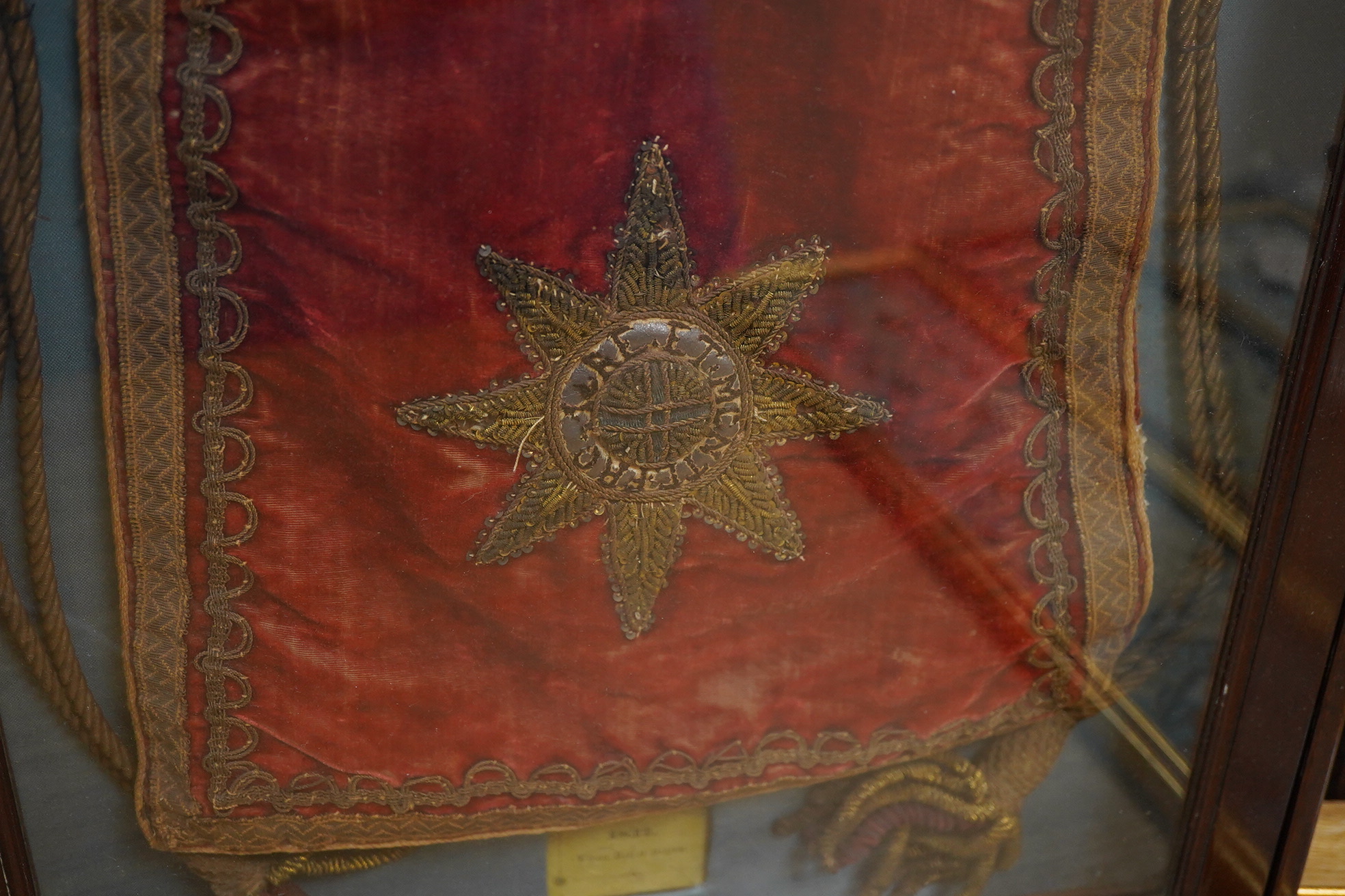 Eton interest - a commemorative William IV, ceremonial red velvet, gold metallic thread, tasselled and braided bag, mounted within a mahogany glazed cabinet. An old printed ticket in Latin mounted beneath: Pro More et Mo